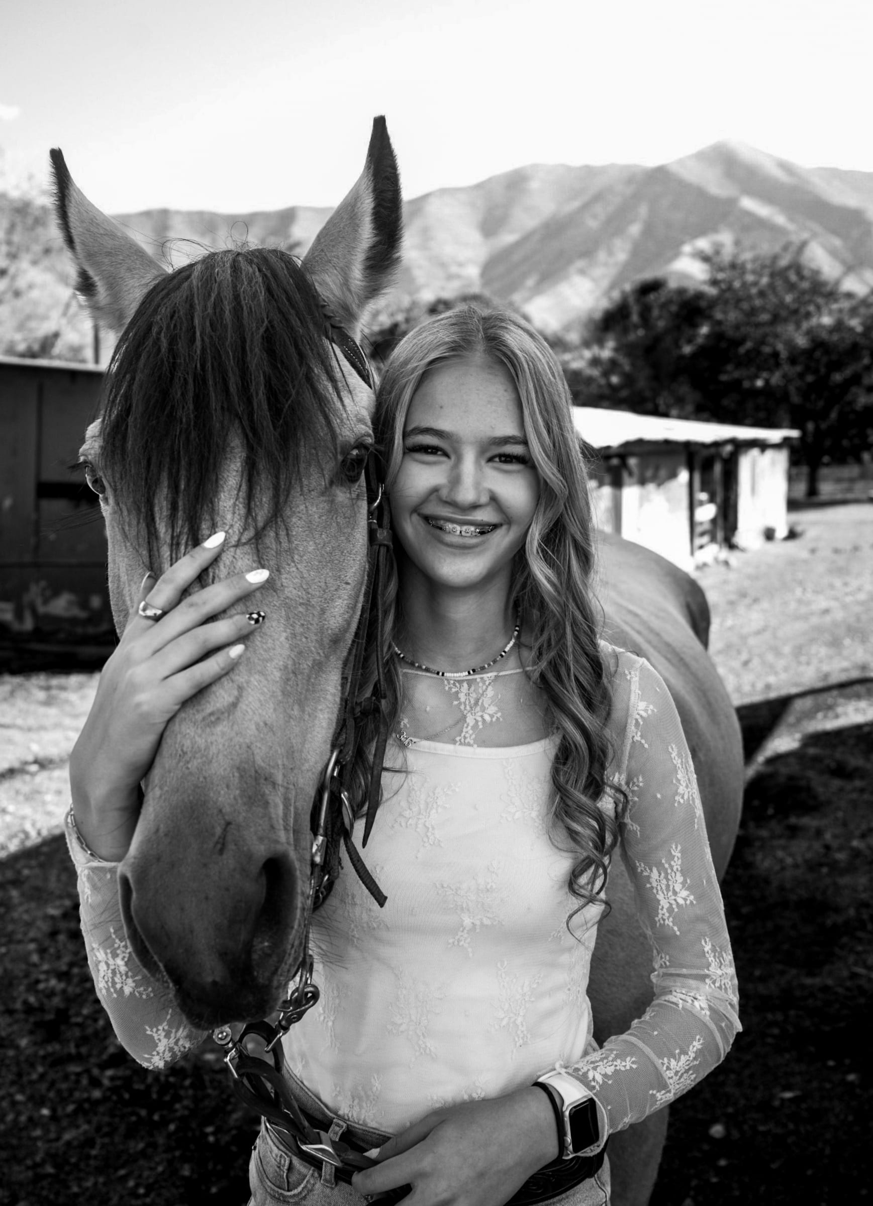 Kennedy with her buckskin horse, mountains behind (black and white)